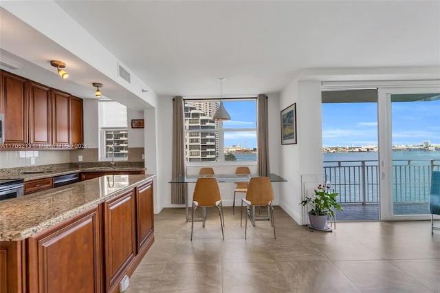 kitchen featuring appliances with stainless steel finishes, light stone counters, sink, decorative light fixtures, and a water view