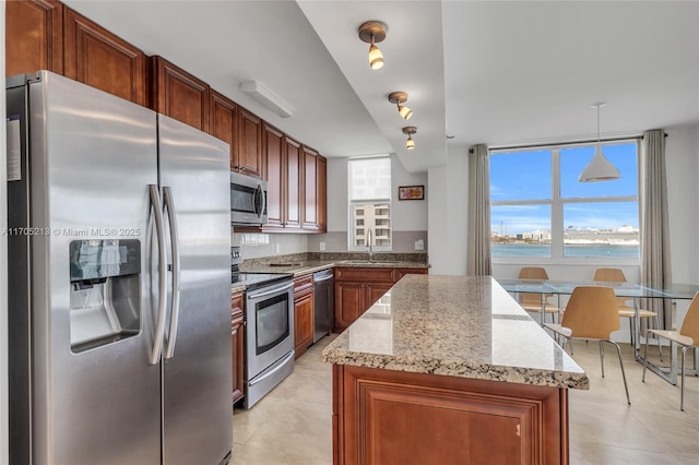 kitchen featuring light stone counters, stainless steel appliances, hanging light fixtures, a sink, and a kitchen island