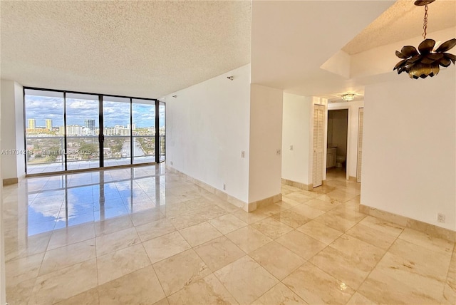 empty room with a textured ceiling, a notable chandelier, baseboards, and expansive windows