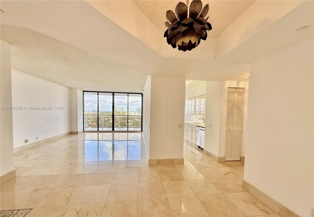 empty room with a wall of windows, a tray ceiling, baseboards, and a textured ceiling