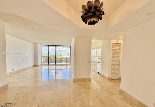 empty room featuring a tray ceiling, floor to ceiling windows, and a textured ceiling