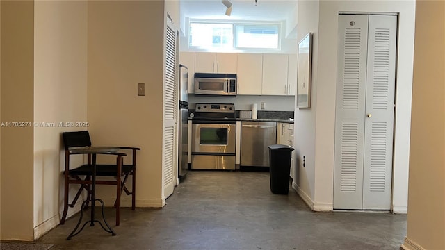 kitchen featuring dark countertops, concrete floors, baseboards, stainless steel appliances, and white cabinetry