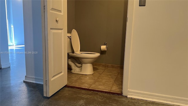 bathroom with toilet, concrete floors, and baseboards