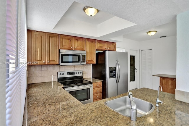 kitchen featuring a raised ceiling, sink, decorative backsplash, light stone countertops, and appliances with stainless steel finishes