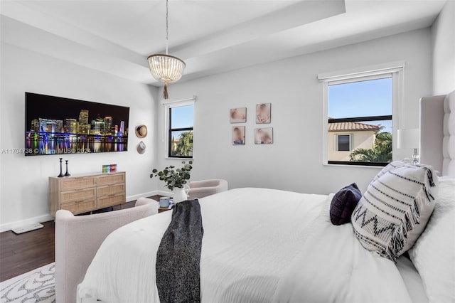 bedroom featuring a raised ceiling, multiple windows, wood-type flooring, and an inviting chandelier