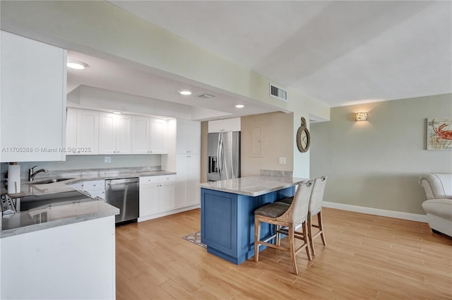 kitchen featuring appliances with stainless steel finishes, light hardwood / wood-style flooring, a breakfast bar area, and white cabinets