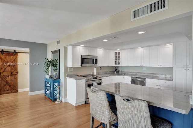 kitchen featuring white cabinetry, stainless steel appliances, light stone counters, and a barn door