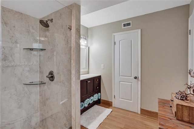 bathroom with hardwood / wood-style flooring, a tile shower, and vanity