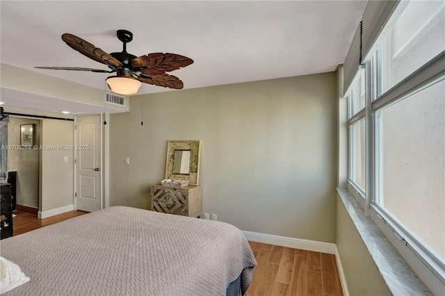 bedroom featuring light hardwood / wood-style floors, ceiling fan, and a barn door