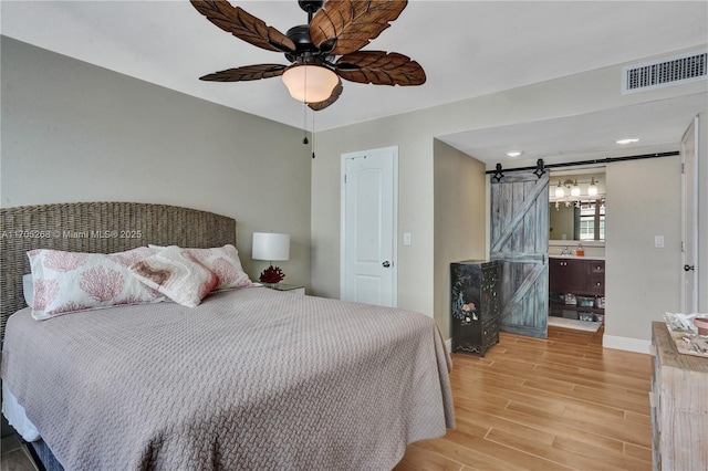 bedroom with light wood-type flooring, ceiling fan, and a barn door