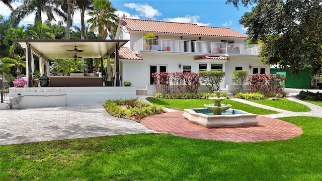 rear view of house with ceiling fan, a yard, french doors, and a balcony