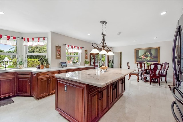 kitchen with a kitchen island, pendant lighting, stainless steel refrigerator, sink, and light stone counters