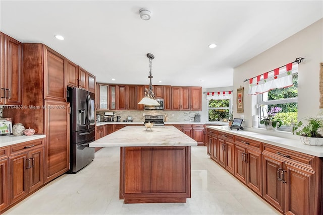 kitchen with appliances with stainless steel finishes, hanging light fixtures, a center island, tasteful backsplash, and light stone counters