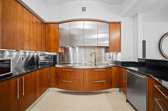 kitchen with backsplash, stainless steel appliances, sink, light tile patterned floors, and dark stone countertops