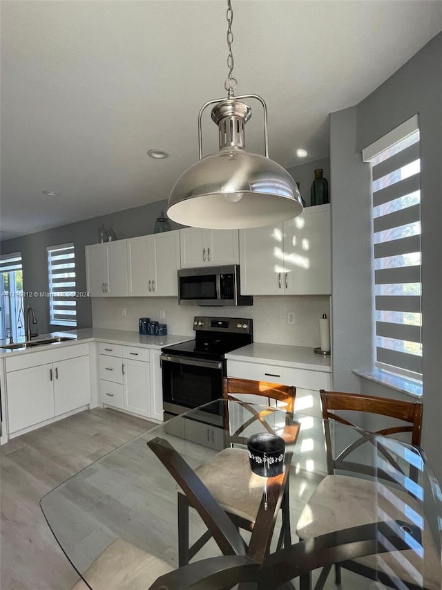 kitchen with sink, tasteful backsplash, decorative light fixtures, white cabinets, and appliances with stainless steel finishes