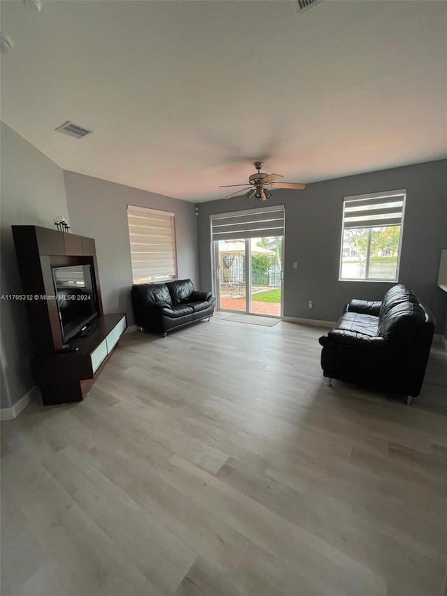 living room with light wood-type flooring, ceiling fan, and a healthy amount of sunlight