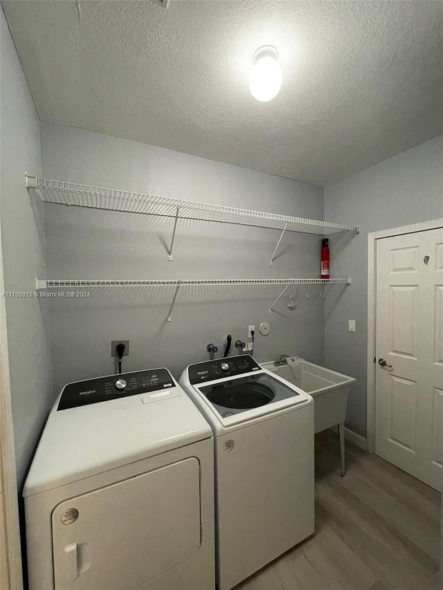 washroom featuring washing machine and dryer, sink, a textured ceiling, and light wood-type flooring