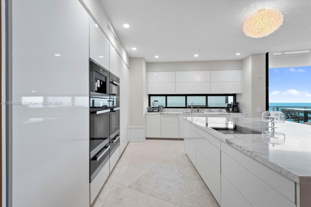 kitchen with a wealth of natural light, white cabinetry, sink, and black electric stovetop