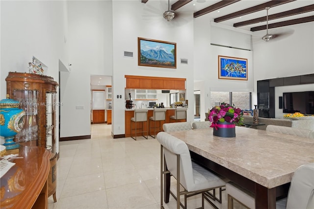 tiled dining space with beamed ceiling, ceiling fan, and a towering ceiling