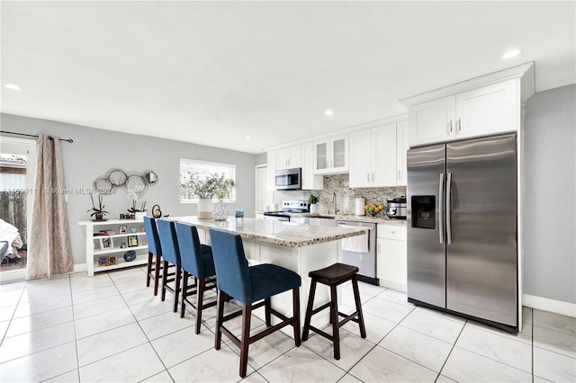 kitchen with light stone countertops, a kitchen breakfast bar, white cabinets, a kitchen island, and appliances with stainless steel finishes