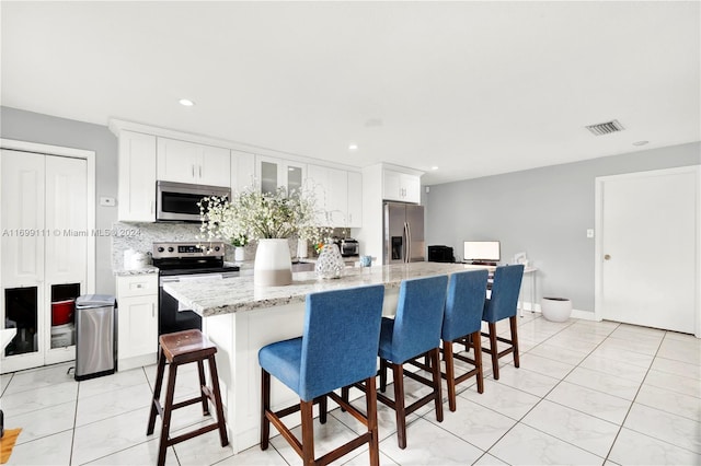 kitchen with appliances with stainless steel finishes, light stone counters, a breakfast bar, a center island, and white cabinetry