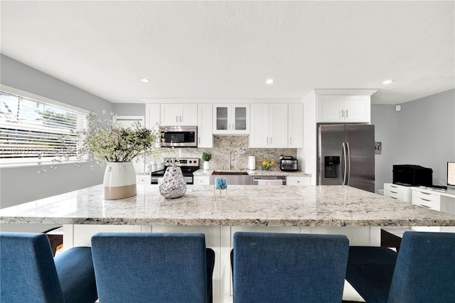 kitchen with a kitchen bar, stainless steel appliances, sink, white cabinets, and a large island