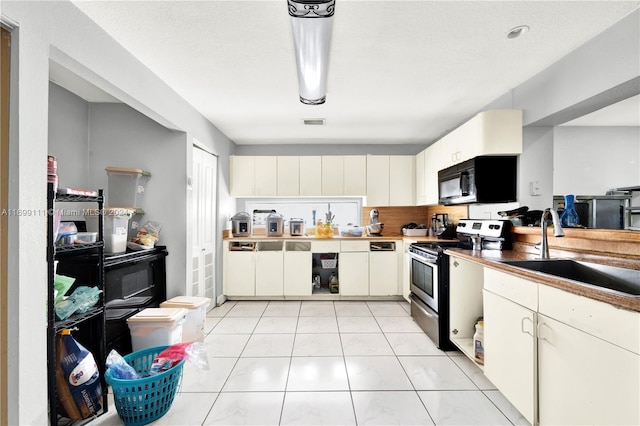 kitchen featuring stainless steel gas range oven, light tile patterned floors, sink, and white cabinetry