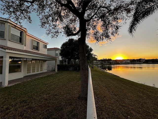 yard at dusk with french doors and a water view