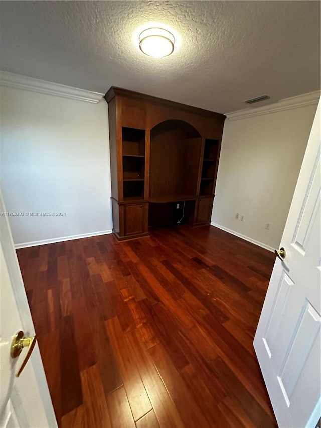 unfurnished living room featuring built in desk, a textured ceiling, crown molding, and dark wood-type flooring