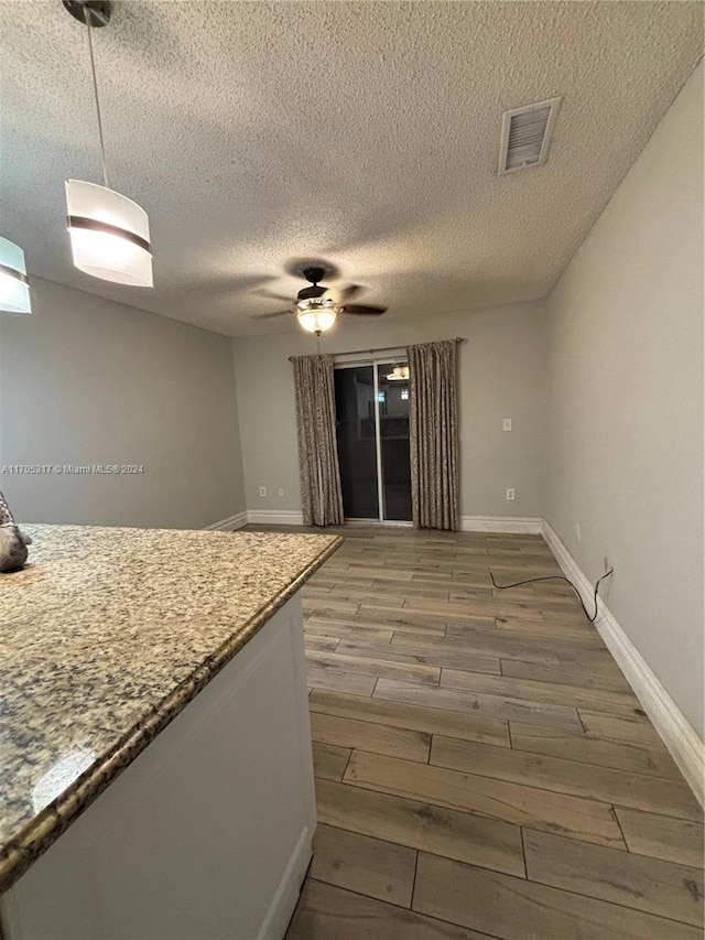 kitchen featuring ceiling fan, hanging light fixtures, wood-type flooring, and a textured ceiling