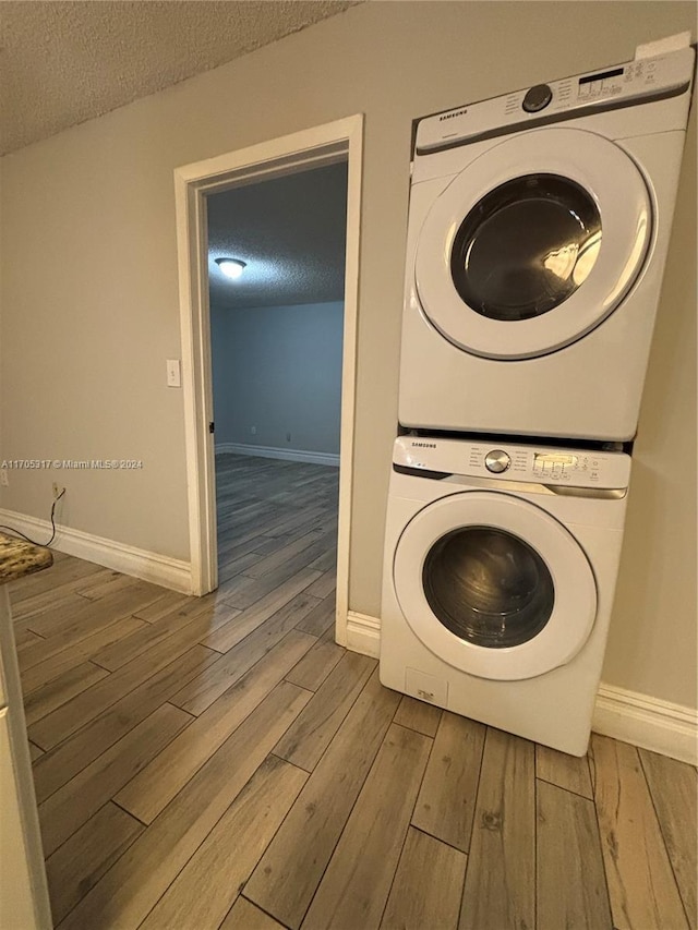 laundry area with a textured ceiling, stacked washer / drying machine, and hardwood / wood-style flooring