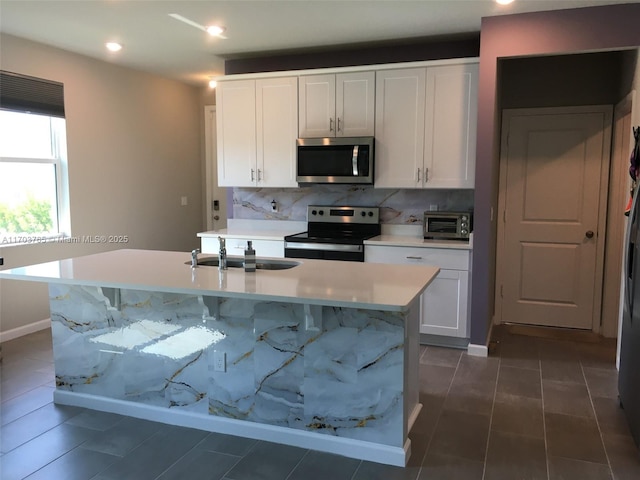 kitchen featuring stainless steel appliances, a center island with sink, light countertops, and white cabinetry