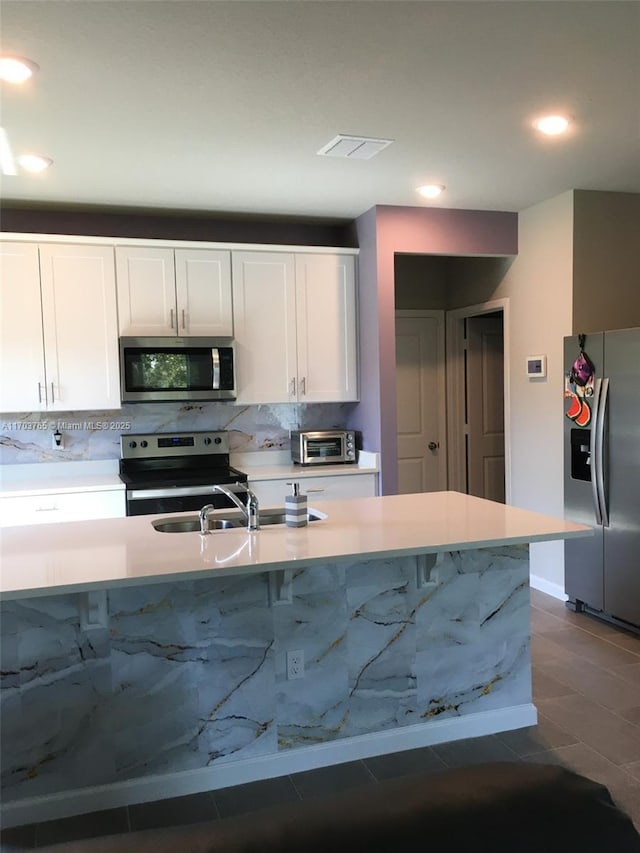 kitchen featuring a toaster, white cabinets, decorative backsplash, appliances with stainless steel finishes, and light countertops