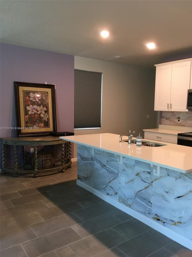 kitchen with light countertops, stainless steel microwave, backsplash, white cabinetry, and a sink