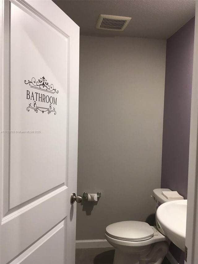 bathroom featuring toilet, a sink, visible vents, and baseboards