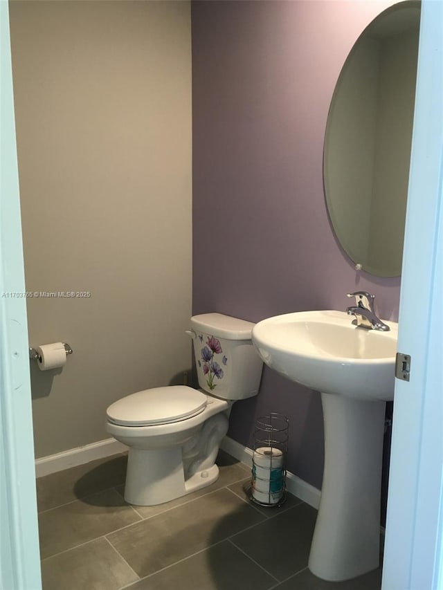 half bath with tile patterned flooring, toilet, and baseboards