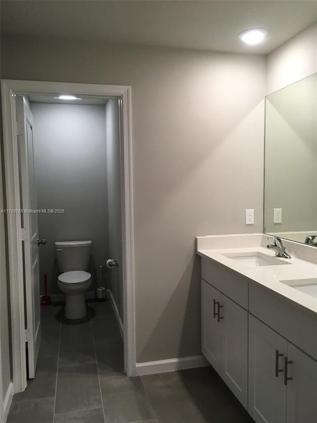 bathroom with tile patterned flooring, toilet, a sink, baseboards, and double vanity