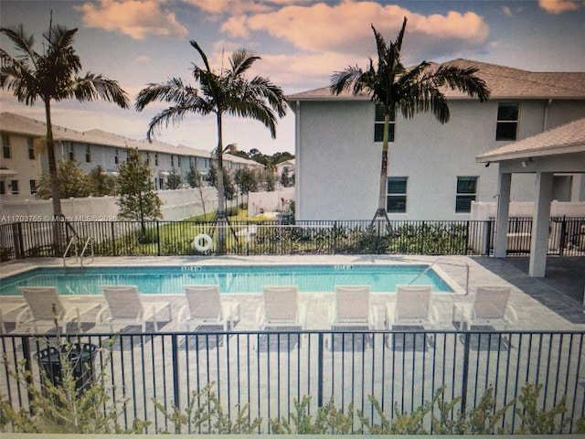 pool at dusk with a patio area, fence, and a community pool