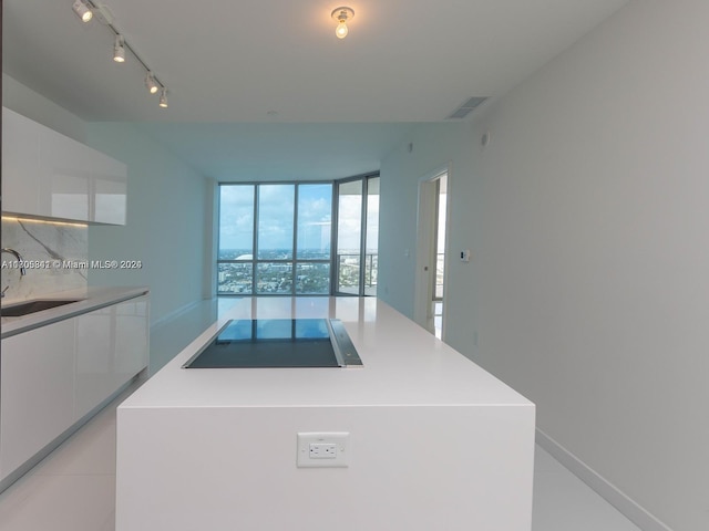 kitchen with black electric stovetop, expansive windows, sink, white cabinets, and a center island