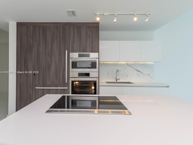 kitchen featuring white cabinetry, sink, stainless steel double oven, tasteful backsplash, and dark brown cabinets