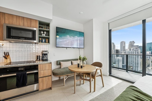 kitchen featuring expansive windows, light stone countertops, light tile patterned floors, tasteful backsplash, and stainless steel appliances