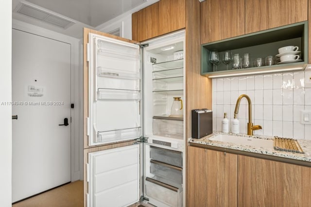 kitchen with backsplash, light stone counters, built in fridge, and sink