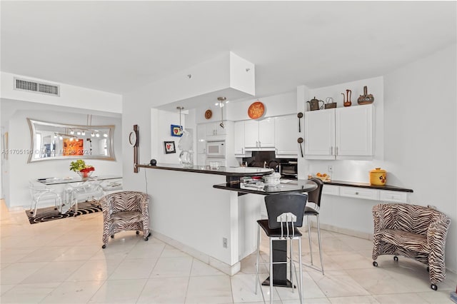 kitchen featuring white cabinetry, light tile patterned floors, kitchen peninsula, a breakfast bar, and white microwave