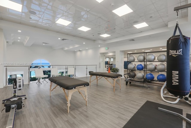 gym featuring a high ceiling, light wood-type flooring, and a drop ceiling