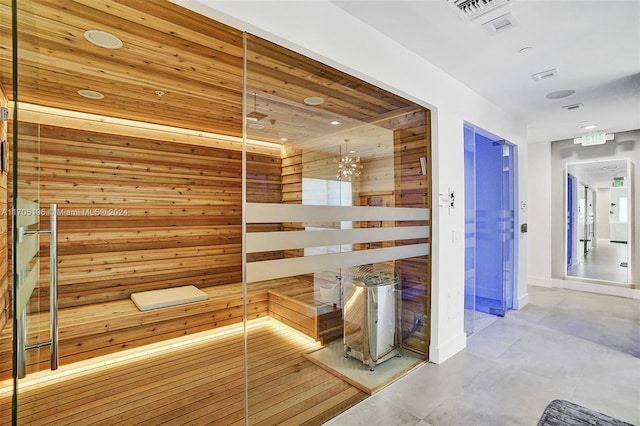 corridor featuring concrete flooring, wooden walls, wooden ceiling, and an inviting chandelier