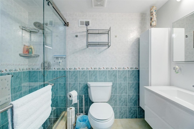 bathroom with tiled shower, vanity, toilet, and tile walls