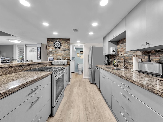 kitchen with gray cabinetry, dark stone counters, sink, appliances with stainless steel finishes, and light hardwood / wood-style floors