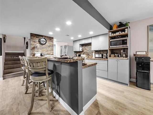 kitchen with dark stone counters, decorative backsplash, stainless steel appliances, and light hardwood / wood-style floors