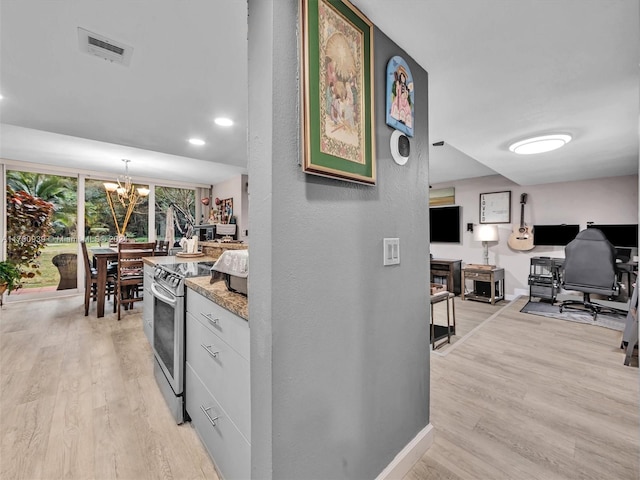 kitchen with stainless steel range with electric stovetop, white cabinets, light wood-type flooring, light stone counters, and a chandelier