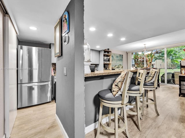 kitchen with a kitchen bar, kitchen peninsula, stainless steel refrigerator, and light hardwood / wood-style flooring